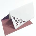 Biglietti pieghevoli decorati con trafori di fiori di mughetto e buste color seppia in carta di Amalfi. Dimensioni busta. 14*9 cm. Dimensioni biglietto: 13*8 cm.